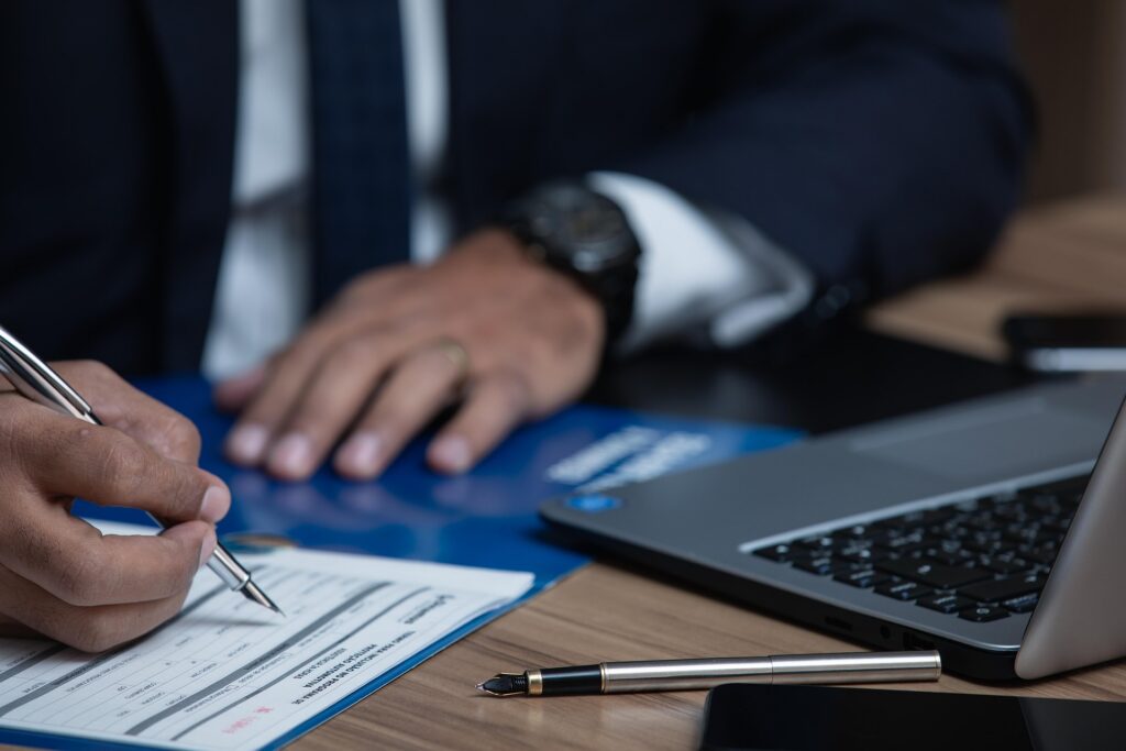 Attorney reviewing and signing legal documents at a desk with a laptop during a client case consultation.