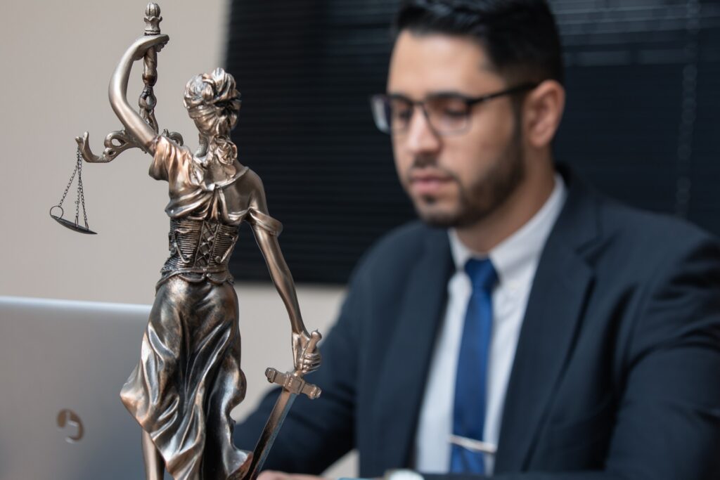 Statue of Lady Justice in the foreground with an attorney working in the background, symbolizing justice and legal representation.