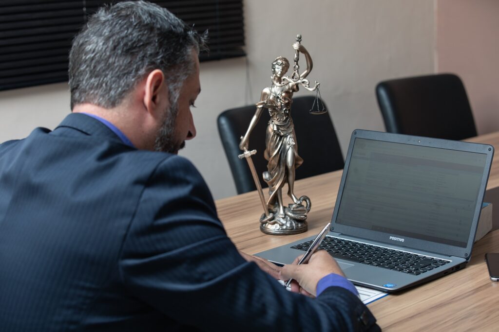 Personal injury lawyer reviewing case documents at a desk with a Lady Justice statue and laptop in the office.