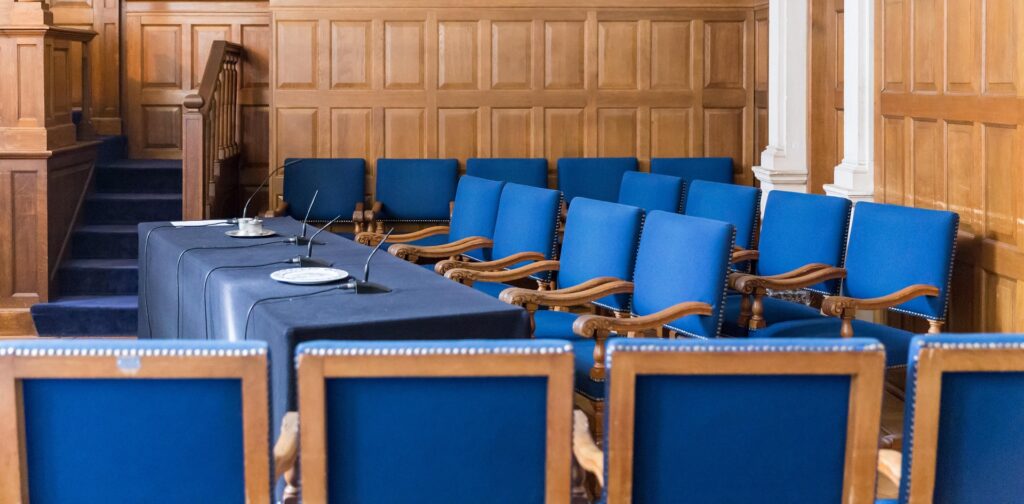 Empty courtroom with jury seating, witness stand, and microphones prepared for a court hearing or trial.