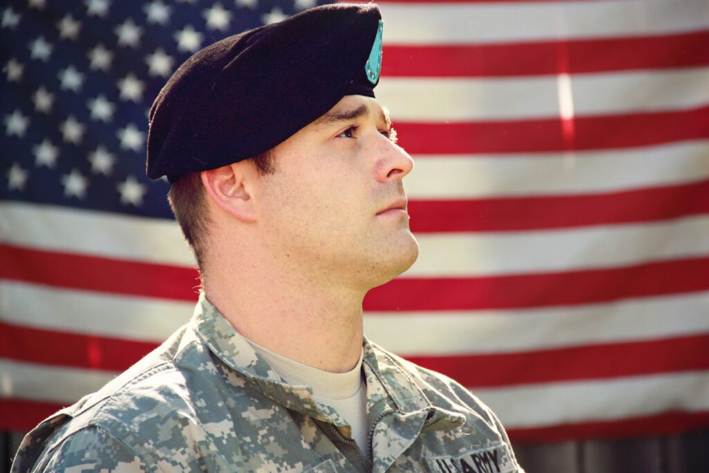 U.S. Army service member standing in front of an American flag during military service.